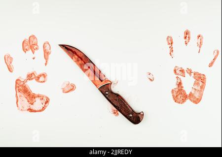 La lama sanguinante e la mano stampano nel sangue su un tavolo bianco. Foto Stock