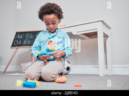 Indovinate cosa sta costruendo... un ragazzo giovane che gioca con i blocchi di costruzione in una stanza. Foto Stock