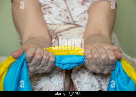 Una vecchia donna tiene la bandiera dell'Ucraina nelle sue mani a casa in Ucraina, fermare la guerra Foto Stock