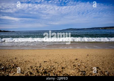 Una vista panoramica delle onde dell'oceano turchese colpendo la spiaggia di sabbia con le colline sullo sfondo Foto Stock
