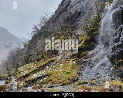 Una vista panoramica di una cascata che scorre sulla montagna rocciosa sotto il cielo grigio Foto Stock