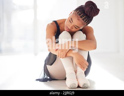 Ci vuole tempo e dedizione per essere bravi a qualsiasi cosa. Una ballerina che guarda triste mentre si siede nel suo studio di danza. Foto Stock