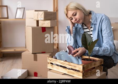 Ritratto di donna moderna infelice in t-shirt vicino scatola di cartone con un piatto rotto sullo sfondo Foto Stock