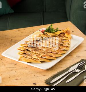 Una pizza turca mince pita Pide su un piatto bianco su un tavolo di legno accanto alle posate Foto Stock