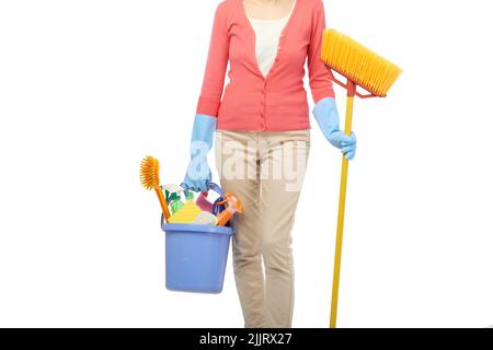 Casalinga non riconoscibile in guanti di gomma che tengono scopa e secchio con utensili di pulizia in mano mentre si trova su sfondo bianco Foto Stock