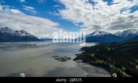 Una vista aerea di una catena montuosa innevata coperta di nuvole contro un lago nella speranza, Alaska Foto Stock