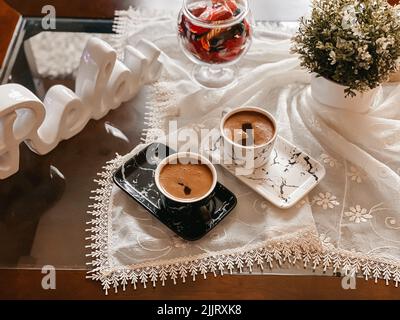 Una vista dall'alto di tazze di caffè ben disposte su una tovaglia decorata con fiori Foto Stock