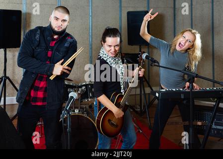 Tre bandmates che si posano insieme a strumenti musicali nella sala delle prove Foto Stock