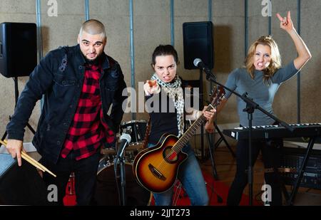 Tre bandmates che si posano insieme a strumenti musicali nella sala delle prove Foto Stock