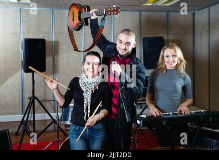 Tre bandmates che si posano insieme a strumenti musicali nella sala delle prove Foto Stock