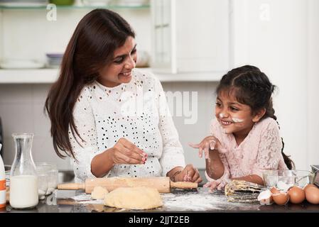 Sorridendo bambina con il viso cosparso di farina guardando via mentre aiutava la sua graziosa madre di mezza età a fare l'impasto per deliziosi cupcakes Foto Stock