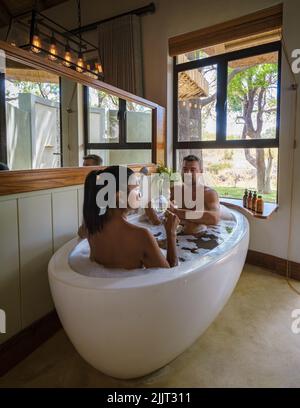 Uomini e donne in una vasca da bagno, una coppia in safari in Sud Africa in un rifugio safari di lusso. Uomini e donne rilassarsi in bagno Foto Stock