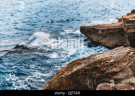 Un'onda oceanica che colpisce enormi rocce sulla riva - perfetto per lo sfondo Foto Stock