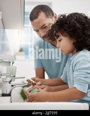 Assicuratevi di disciplinare i bambini sulla pulizia. Un padre che aiuta suo figlio a lavarsi le mani a un rubinetto in un bagno a casa. Foto Stock