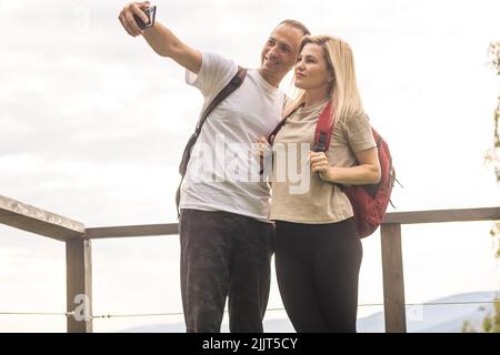 Orizzontale vista laterale di una giovane coppia in abito estivo godendo la vista della montagna dalla terrazza. Spazio di copia. Foto Stock