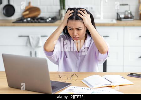 Giovane donna freelance che guarda preoccupata lo schermo del laptop che tiene la testa che legge le cattive notizie sul email Foto Stock