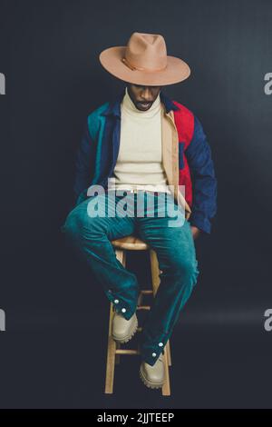 Un uomo afro-americano dagli Stati Uniti in un cappello e vestito casual in posa in uno studio fotografico Foto Stock