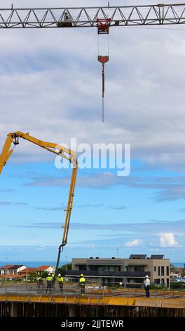 I lavoratori edili pettinano il calcestruzzo appena versato da un braccio pompato sul nuovo pavimento di un blocco di appartamenti Santander Cantabria Spagna Foto Stock