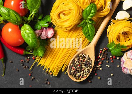 Spaghetti e tagliatelle con pomodori pepe aglio e prezzemolo su sfondo scuro vista dall'alto ingredienti italiani Foto Stock