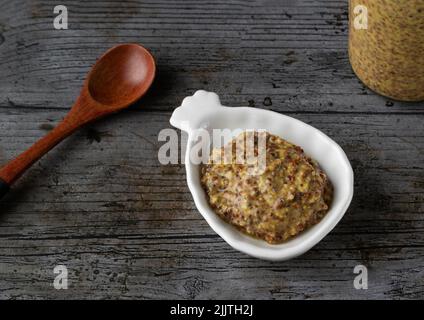 Senape vecchia su un piatto bianco su sfondo rustico Foto Stock