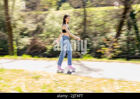 donna bruna pattinare in un parco con pattini a rotelle rosa Foto Stock