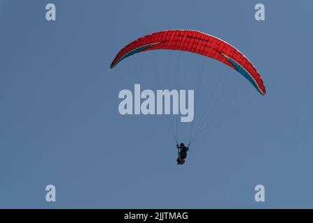 Un'inquadratura a basso angolo di un parapendio che vola nel cielo azzurro con un paracadute rosso Foto Stock