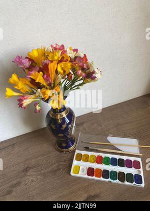 Un colpo verticale di fiori in vaso e acquerello vernice set su un tavolo di legno Foto Stock