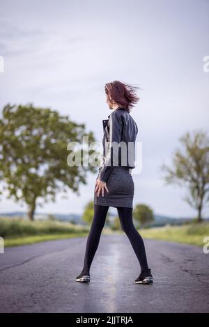 Una bella foto di una giovane donna che cammina su una strada che attraversa campi verdi in una giornata di sole Foto Stock