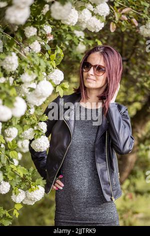 Una bella giovane donna caucasica in piedi da alberi in fiore in un giardino in una giornata di sole Foto Stock