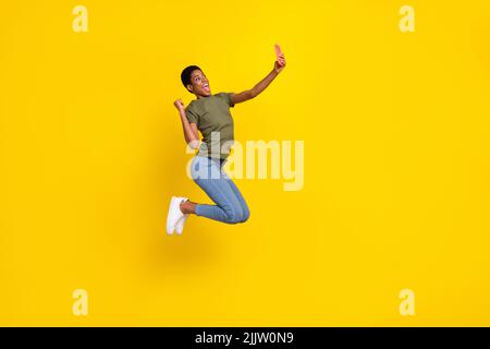 Foto a grandezza naturale di entusiasta persona eccitata sollevare pugno salto prendere selfie foto isolato su sfondo giallo Foto Stock