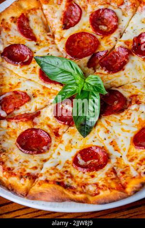 Primo piano verticale di una classica pizza al peperone servita con foglie di basilico. Foto Stock