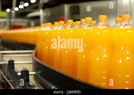 Produzione di bevande gassate. Bottiglie arancioni sulla linea di produzione Foto Stock