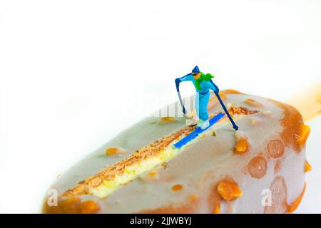 lo sciatore scivolerà giù su un popsicle al cioccolato, sfondo bianco Foto Stock