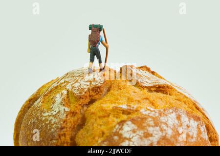escursionista con bastone e zaino si alza su un pane fresco, sfondo bianco Foto Stock