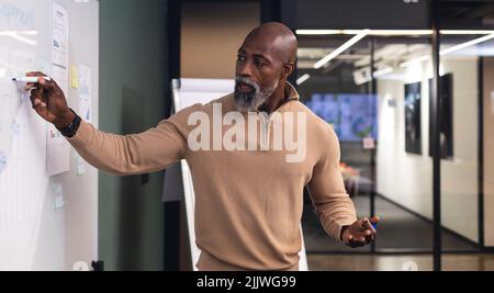 Uomo d'affari maturo afro-americano che spiega la strategia di affari sopra la lavagna bianca Foto Stock