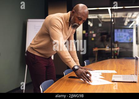 Uomo d'affari maturo afro-americano che analizza i documenti alla scrivania in ufficio Foto Stock