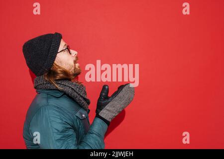 Uomo zenzero che indossa cappello e giacca tremante e sensazione di freddo isolato su sfondo rosso Foto Stock