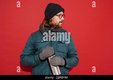 Uomo bianco che indossa abiti caldi aprendo i suoi thermos isolato su sfondo rosso Foto Stock