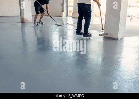 Due operai edili che applicano resina epossidica grigia in un ambiente industriale Foto Stock