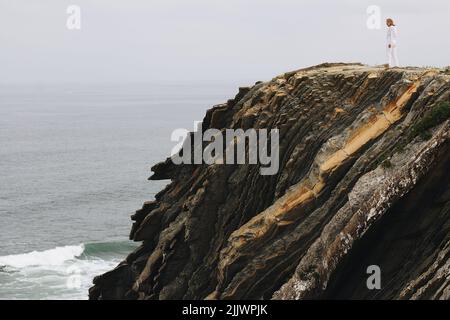 Una vista sul mare e la donna in piedi su una scogliera rocciosa Foto Stock