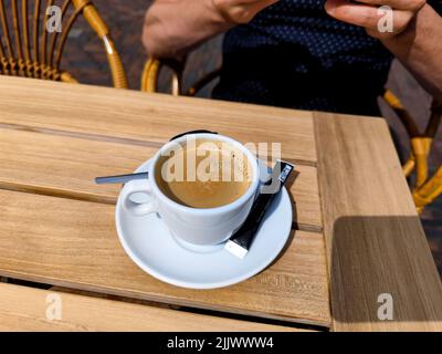 Tazza di caffè appena preparata con un sacchetto di zucchero, una tazza di latte di caffè e un cucchiaio su un tavolo in legno da terrazza. Non ci sono persone o marchi negli Foto Stock