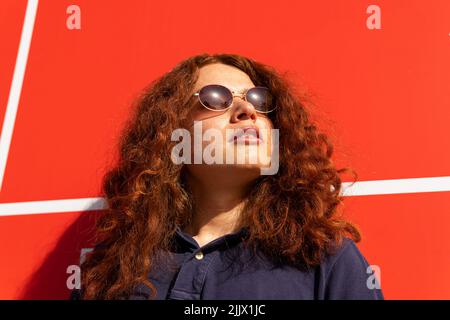 Ritratto della giovane donna che indossa occhiali da sole in piedi contro il muro Foto Stock