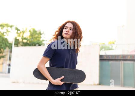 Ritratto di giovane donna con skateboard in piedi in città Foto Stock