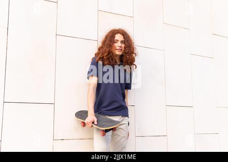 Giovane donna allegra con Skate contro il muro bianco della città Foto Stock