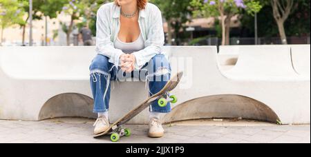 Donna ritagliata e irriconoscibile in abbigliamento casual con skateboard guardando lontano mentre si siede nel parco skate in città Foto Stock