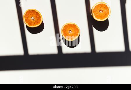 Vista dall'alto delle metà delle arance schiacciate poste su un tavolo bianco vicino all'ombra della ringhiera al mattino soleggiato Foto Stock