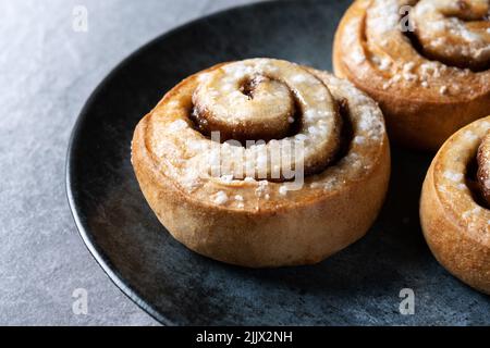 Panini alla cannella Kanelbulle tradizionale dessert svedese servito in piatto nero Foto Stock