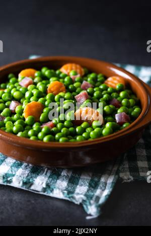 Ciotola di deliziosi piselli verdi con prosciutto e carota posta su tovagliolo su sfondo scuro Foto Stock