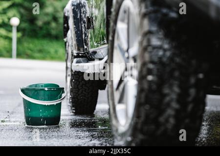 Auto nera coperta con schiuma per lavaggio e bolla di sapone sulla cappa accanto al secchio Foto Stock