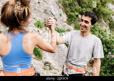 Coppia di escursionisti allegri che tengono le mani mentre si alza sulla scogliera durante le escursioni Foto Stock